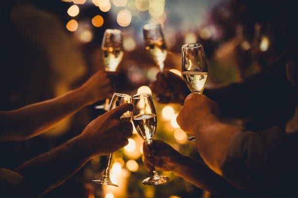 Group of people toasting with champagne glasses at a celebration, with warm lighting in the background.